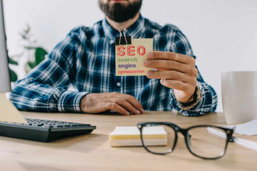 cropped shot of young bearded developer holding sticker with SEO - search engine optimization