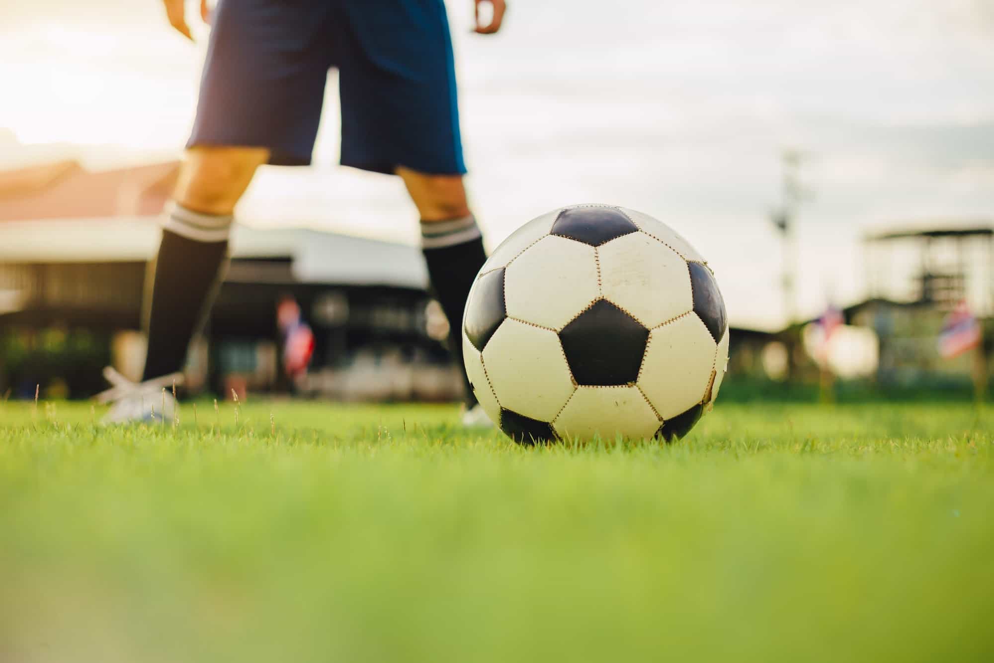 Sport man tying shoes with classic ball before playing soccer football on green grass field. Athlete