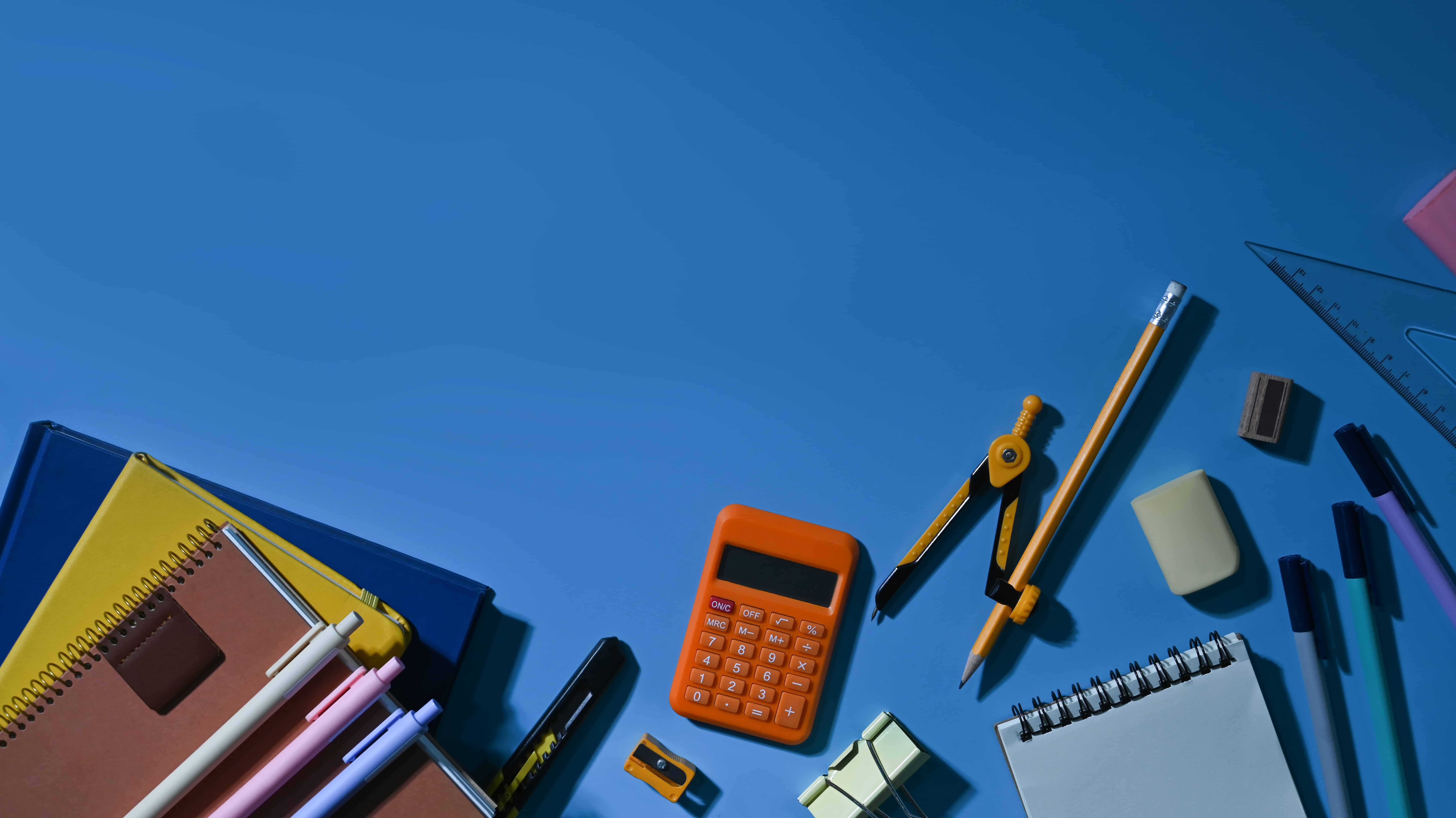Top view of various school supplies on a blue background with empty space ready for your design.